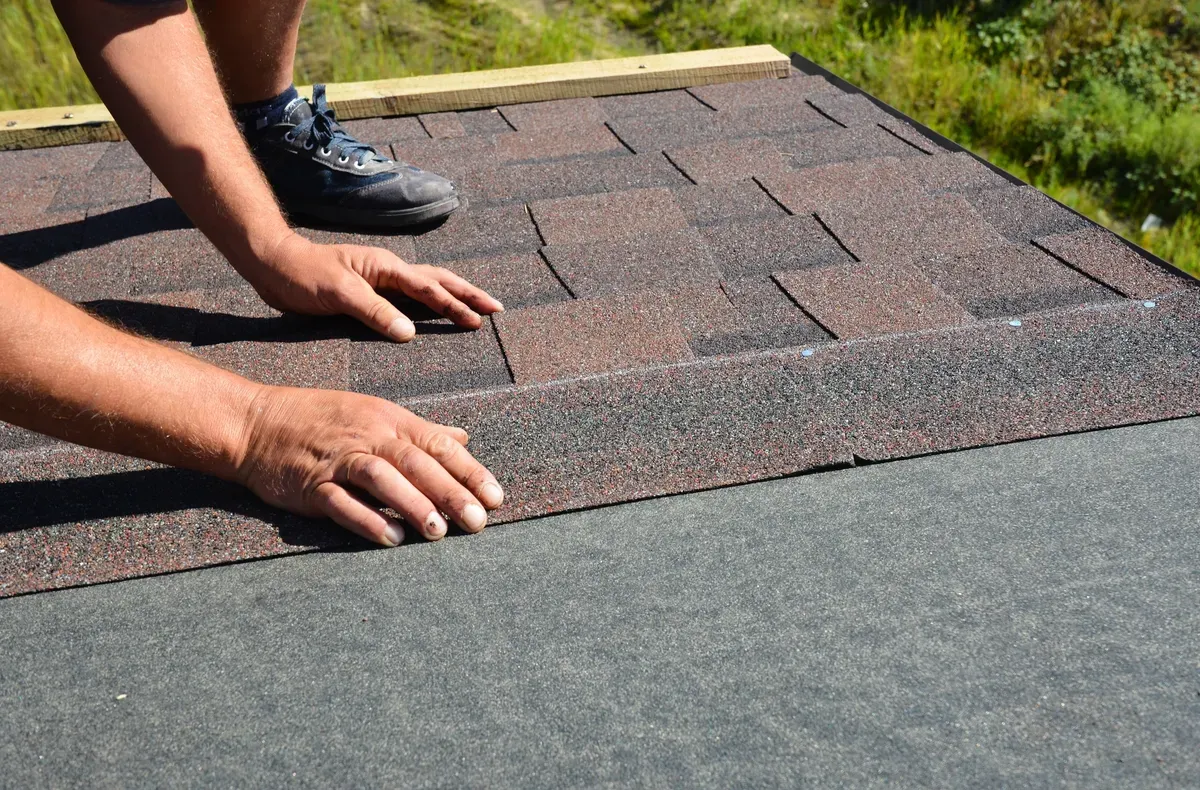 Person installing asphalt roof shingles.